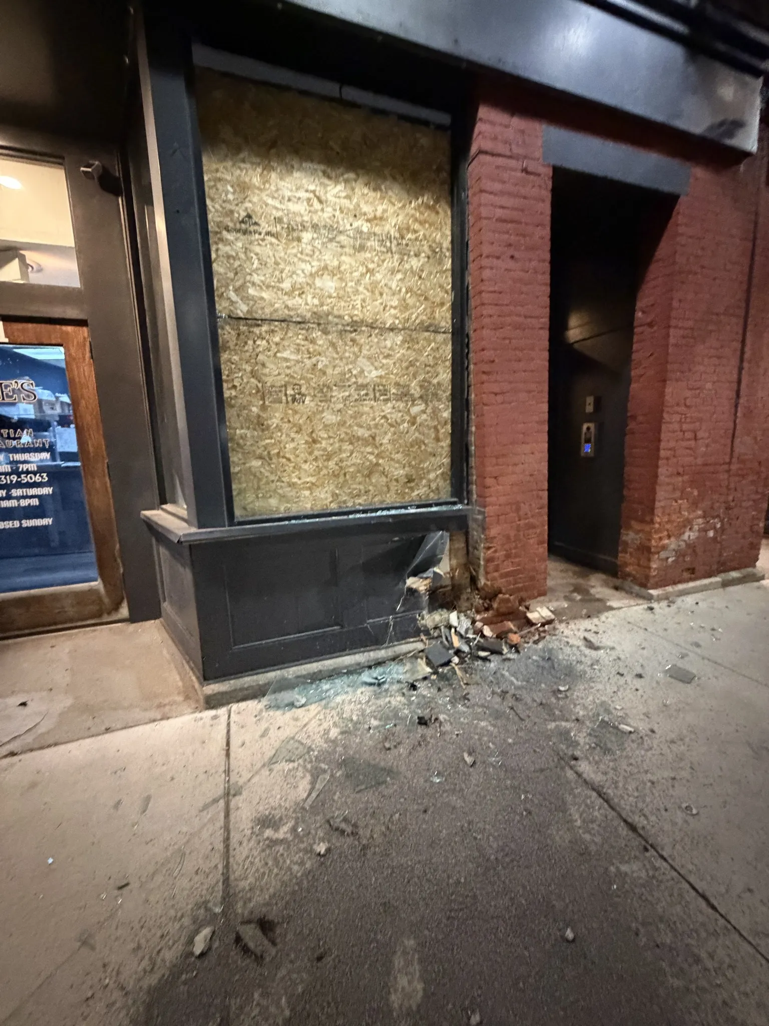 Storefront window boarded up after glass damage in downtown building