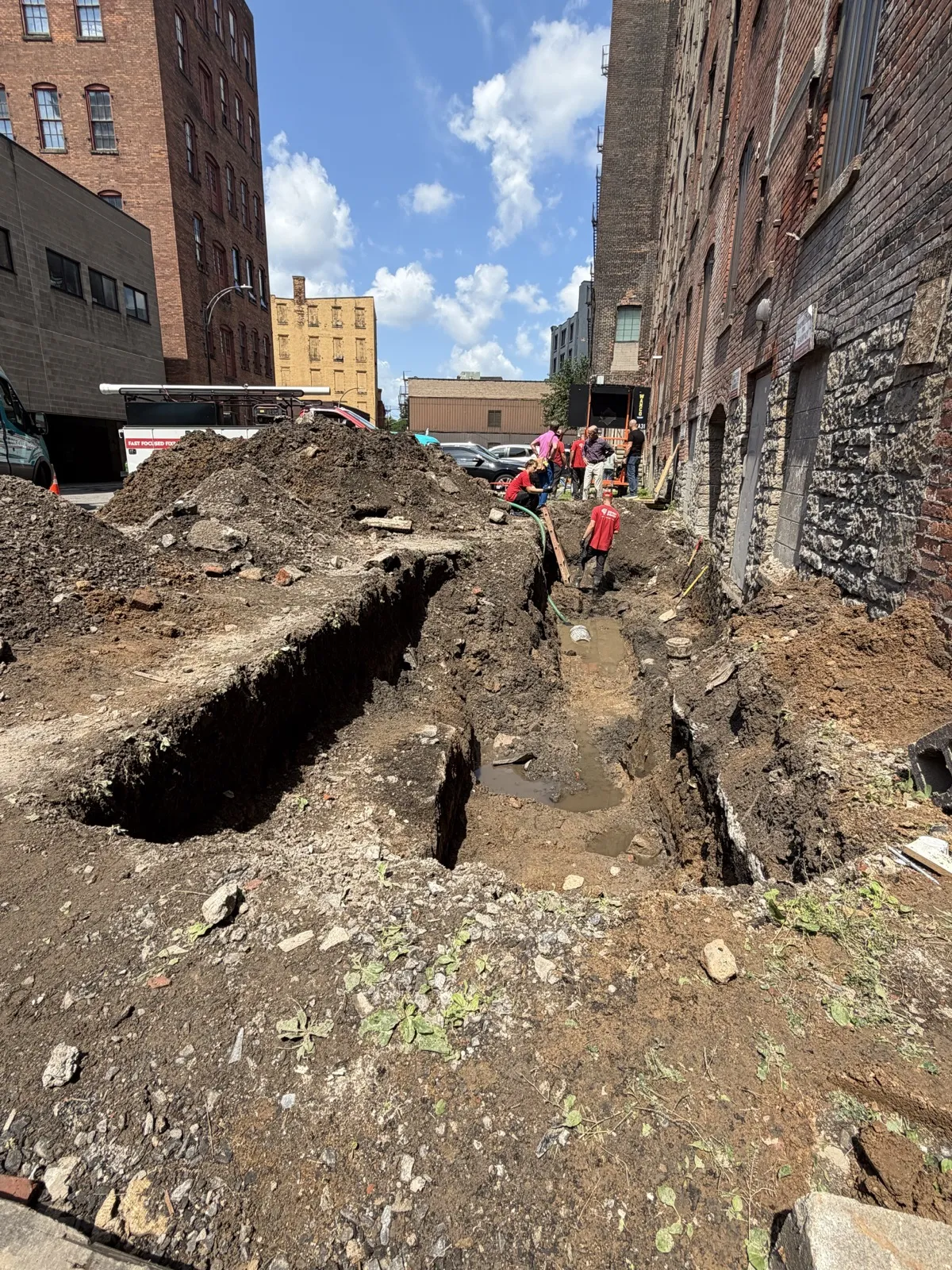 Deep excavation trench alongside brick building in urban alley